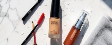 Produits de maquillage waterproof disposes sur une surface en marbre sous une lumiere estivale avec des gouttes d eau