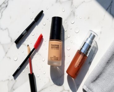 Produits de maquillage waterproof disposes sur une surface en marbre sous une lumiere estivale avec des gouttes d eau