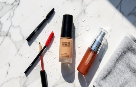 Produits de maquillage waterproof disposes sur une surface en marbre sous une lumiere estivale avec des gouttes d eau