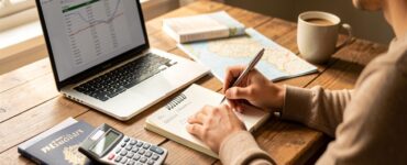 Personne planifiant un budget voyage sur ordinateur portable avec carnet et calculatrice